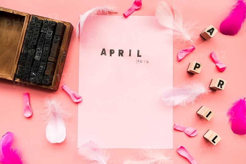 Wooden typographic blocks balloons feather april blocks april stamp white paper against pink backdrop