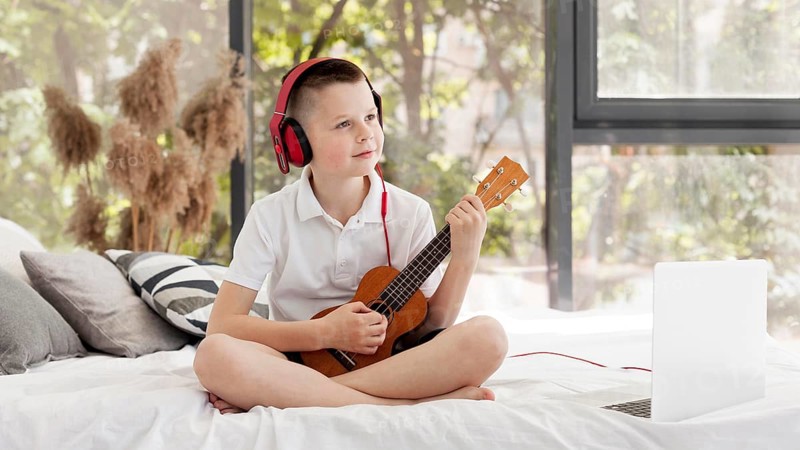 Boy with headphones playing ukulele long shot