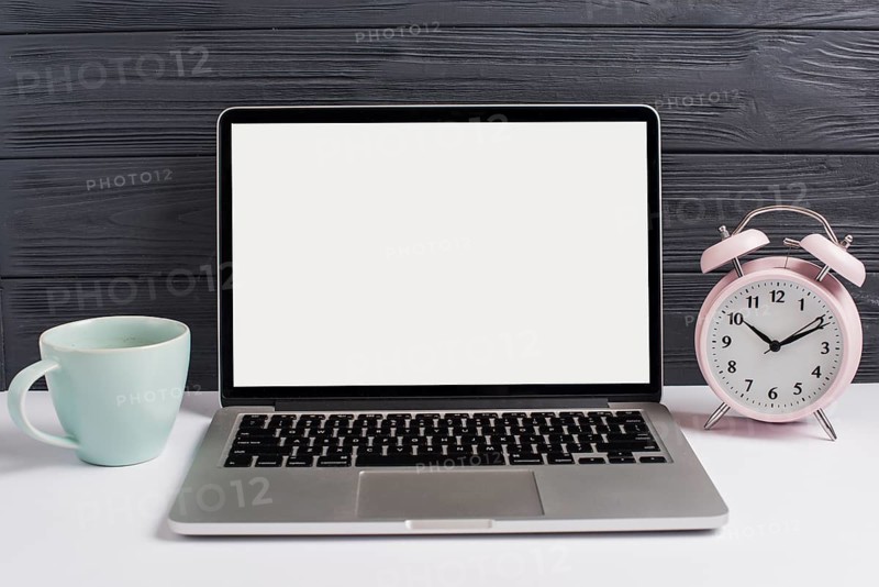 Ceramics cup alarm clock open laptop white desk against wooden black background
