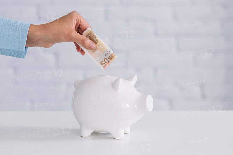 Close up person s hand inserting fifty euro banknote piggybank desk