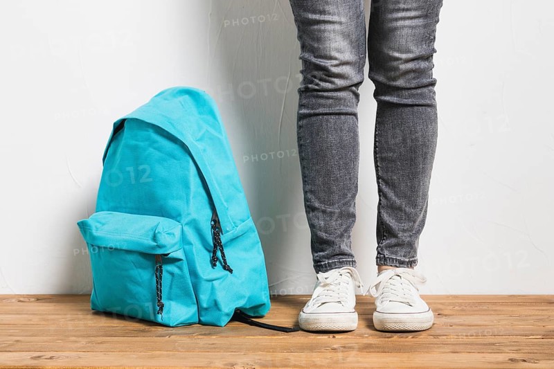 Faceless person standing beside schoolbag wooden table