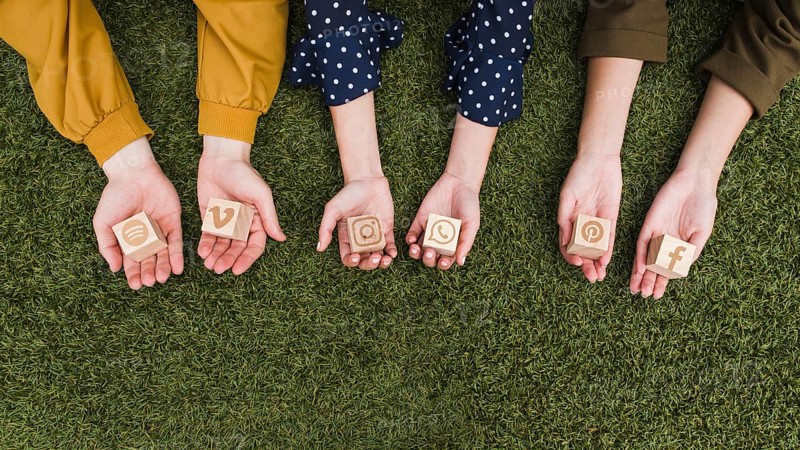 Hand s holding social media app icons wooden blocks green grass