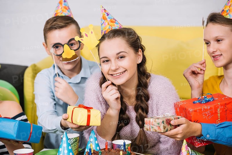 Happy friends holding props hand giving gifts smiling teenage girl