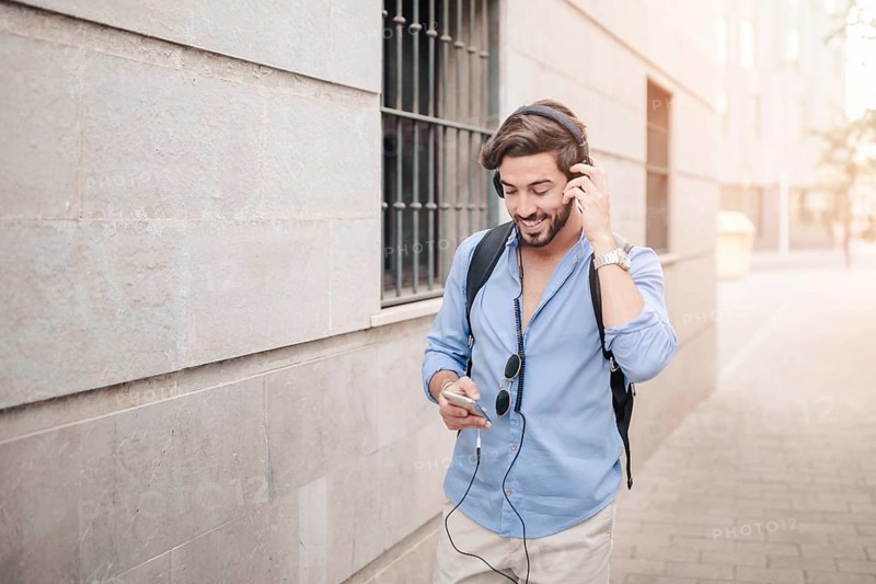 Happy man walking pavement listening music