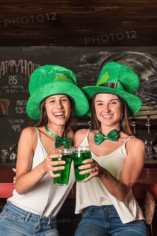 Laughing young women saint patricks hats hugging holding glasses drink bar counter