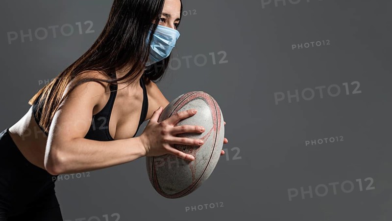 Side view athletic female rugby player holding ball while wearing medical mask
