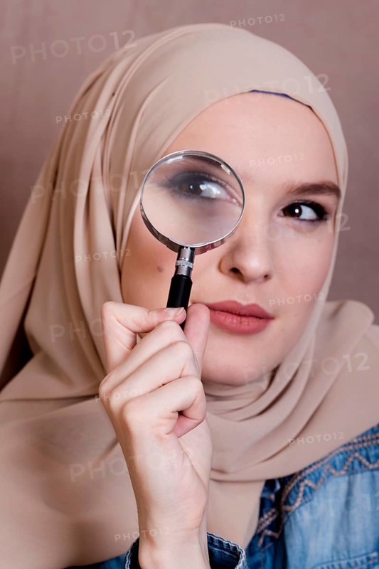 Close up curious muslim woman looking through magnifying glass