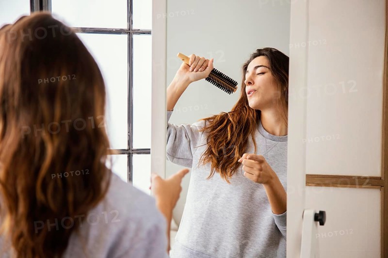 Front view happy woman singing into hairbrush home
