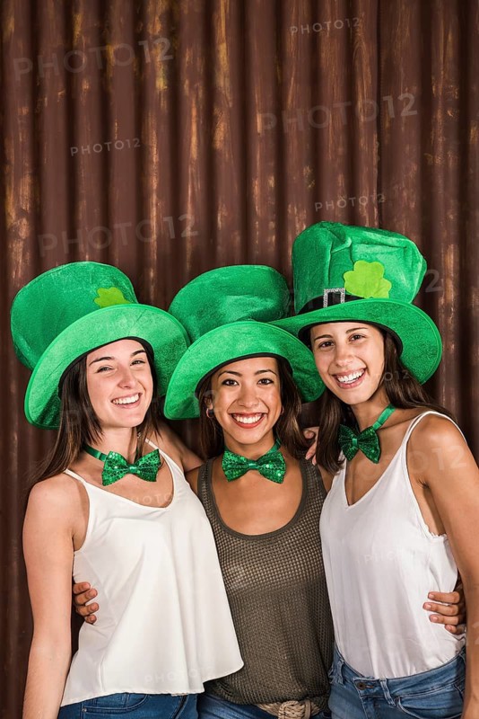 Happy young women saint patricks hats hugging near wall