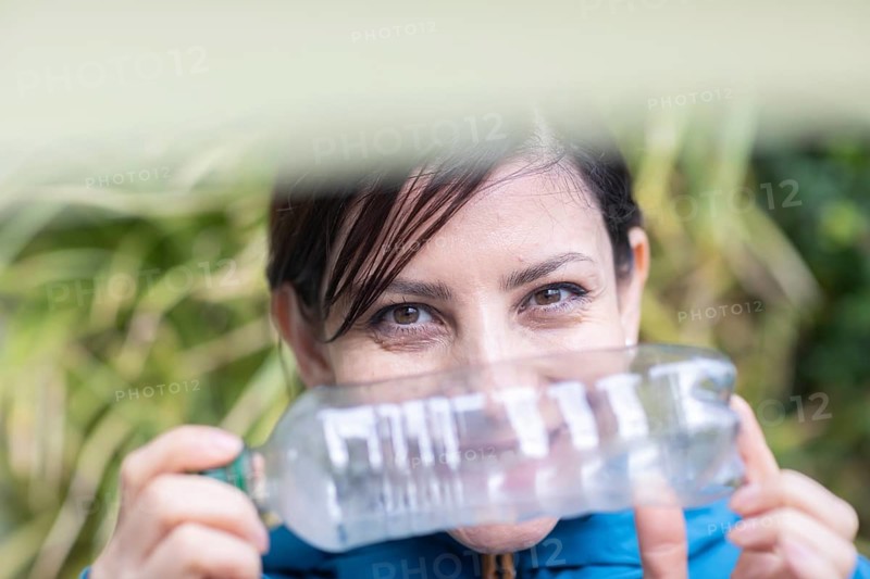 Woman with a plastic bottle in front of a wall of plants Environmental protection