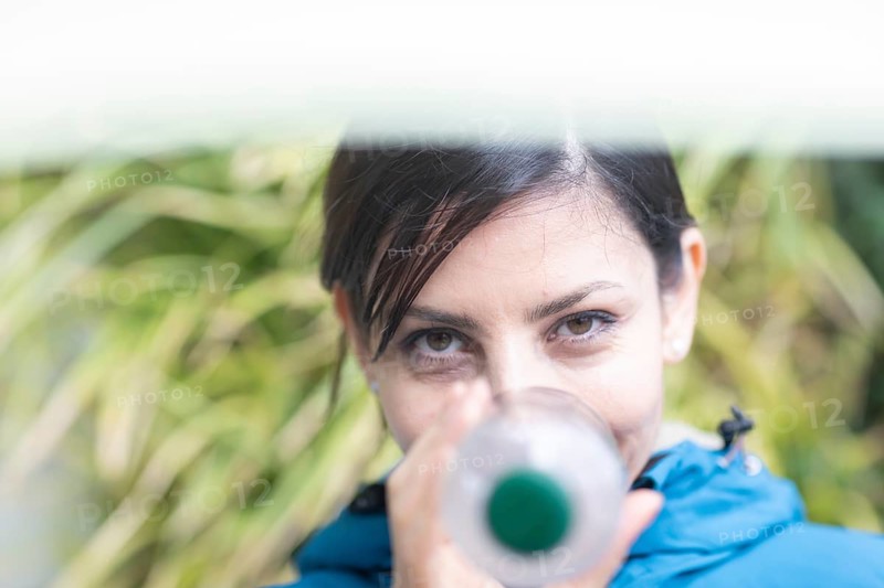 Woman with a plastic bottle in front of a wall of plants Environmental protection