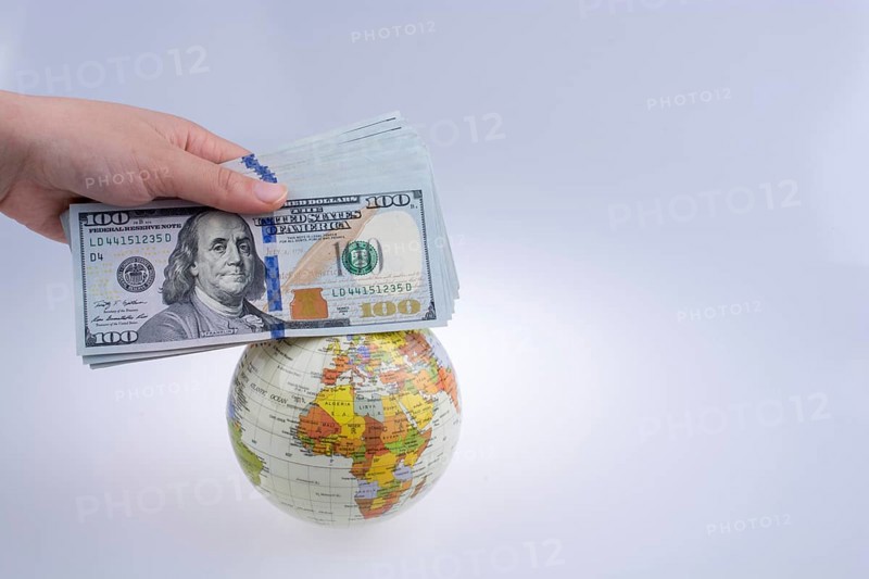 Human hand holding American dollar banknotes by the side of a model globe on white background