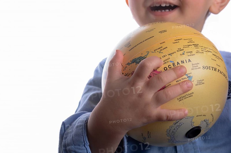 Baby with blue shirt holding a globe in hand on white background