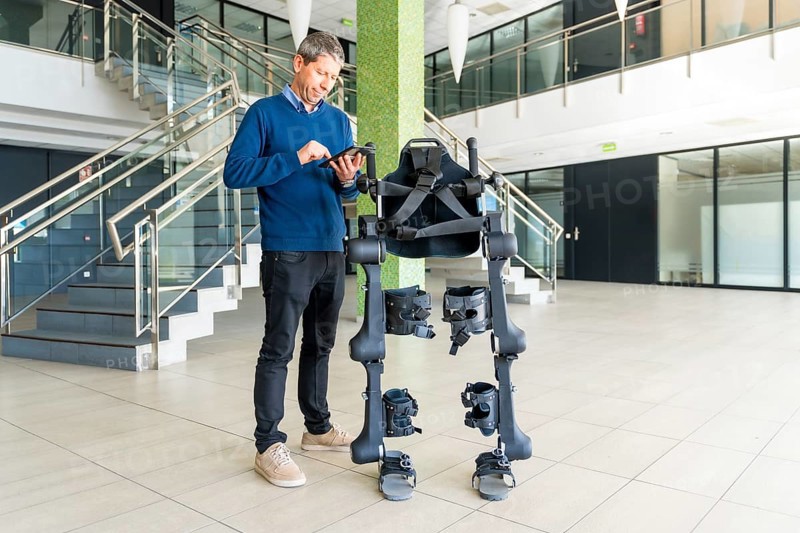 Mechanical exoskeleton computer engineer looking at the robot with a tablet. Physiotherapy in a modern hospital: Robotic skeleton. Physiotherapy Rehabilitation Scientists