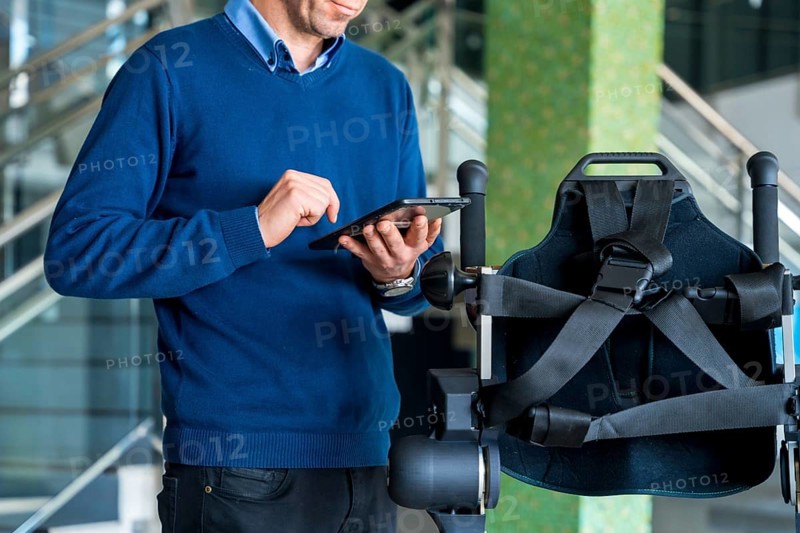 Unrecognizable computer engineer in mechanical exoskeleton looking at the robot with a tablet. Physiotherapy in a modern hospital: Robotic skeleton. Physiotherapy Rehabilitation Scientists