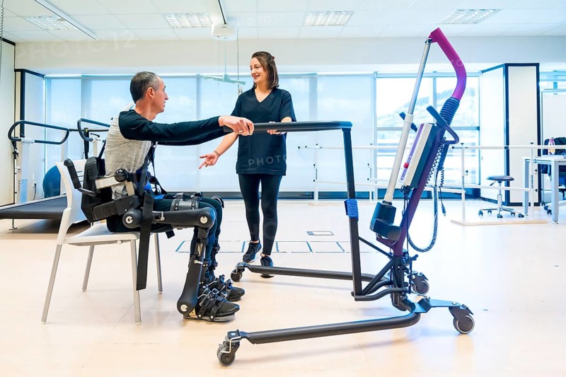 Mechanical exoskeleton. Physiotherapy assistant lifting disabled person with robotic skeleton to get up. Futuristic rehabilitation