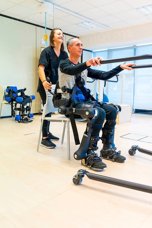 Mechanical exoskeleton. Female physiotherapy doctor assistant lifting disabled person with robotic skeleton to get up. Futuristic rehabilitation