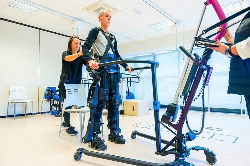 Mechanical exoskeleton. Female physiotherapy medical assistant lifting disabled person with robotic skeleton. Futuristic rehabilitation