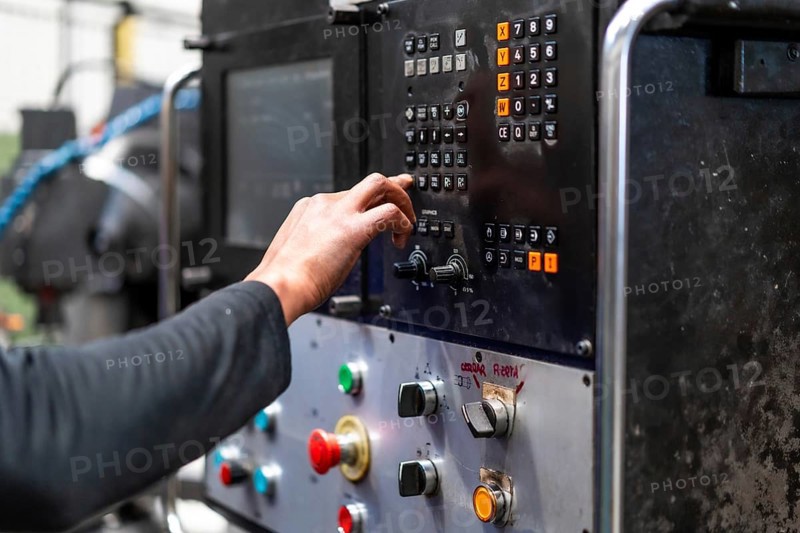 Unrecognizable operator touching the panel of a numerically controlled metal industrial factory machine