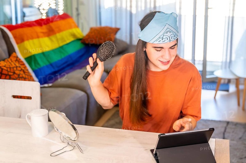 Transgender person brushing the long hair while using tablet sitting on the living room