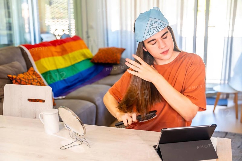 Gay man with long hair brushing it in the living room and using tablet