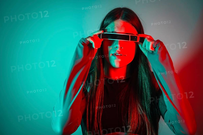 Futuristic studio portrait with neon lights of a transgender person with long hair using smart googles