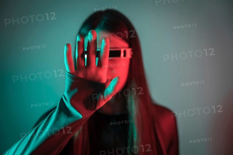 Futuristic studio portrait with neon lights of a transgender person gesturing while using augmented reality smart goggles