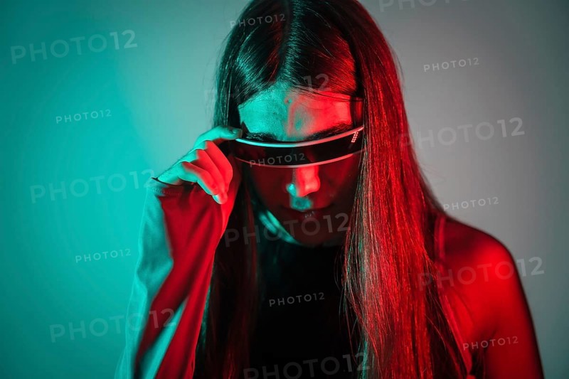 Studio portrait with neon lights of a curious futuristic transgender person using smart goggles