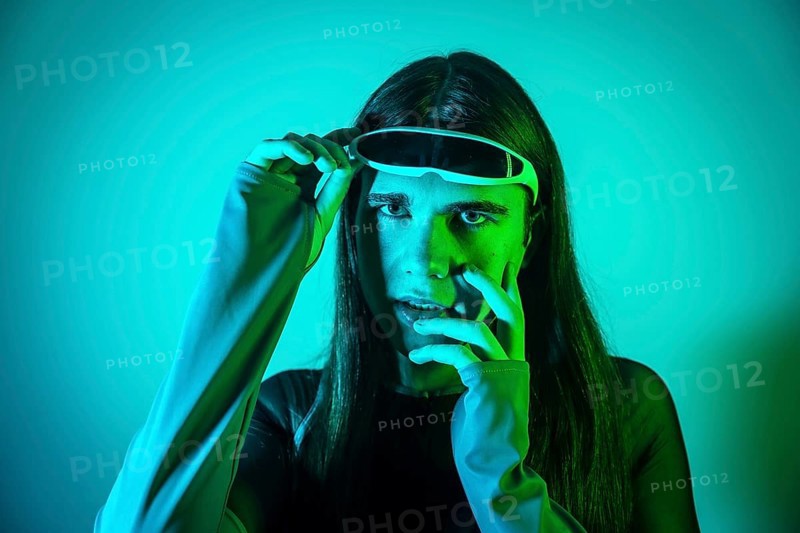 Studio portrait with neon lights of a surprised transgender non binary person using augmented reality futuristic goggles