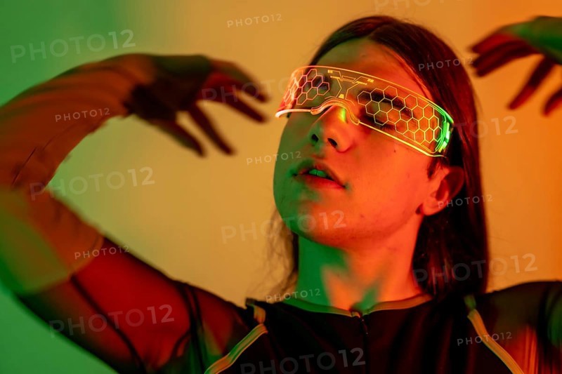 Futuristic studio portrait with neon lights of a sensual non-binary person gesturing while using virtual reality goggles