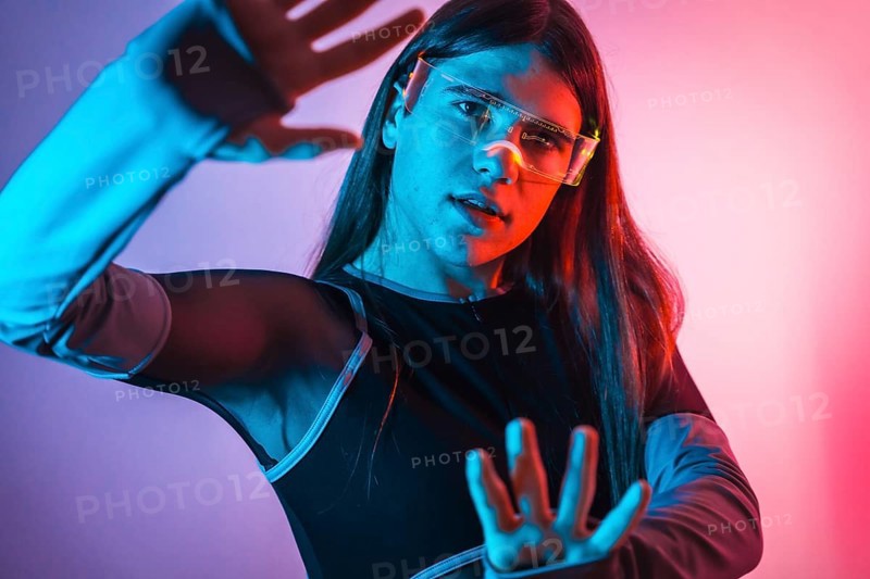 Futuristic studio portrait with neon lights of a transgender person experimenting in the metaverse using augmented reality goggles