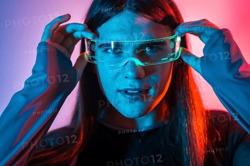 Futuristic studio portrait with neon lights of a non-binary person putting on augmented reality goggles