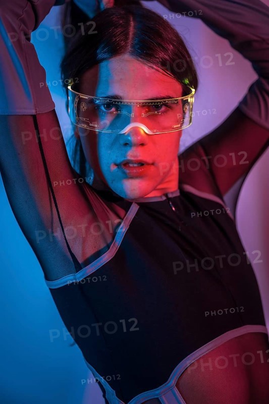 Studio portrait with neon lights of a transgender person posing sensually while using futuristic goggles