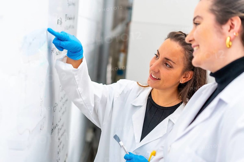 Scientist reading data from a white board in a laboratory next to a colleague
