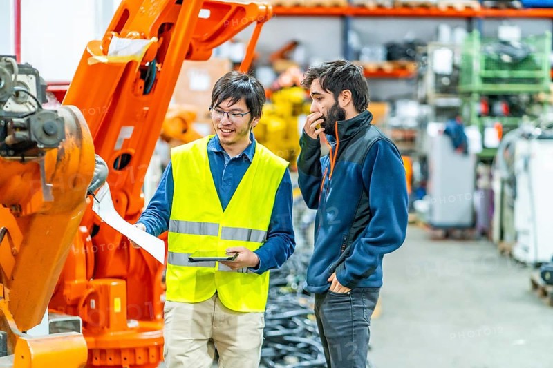 Software engineer explaining to controlling robotic welding process to welder in factory