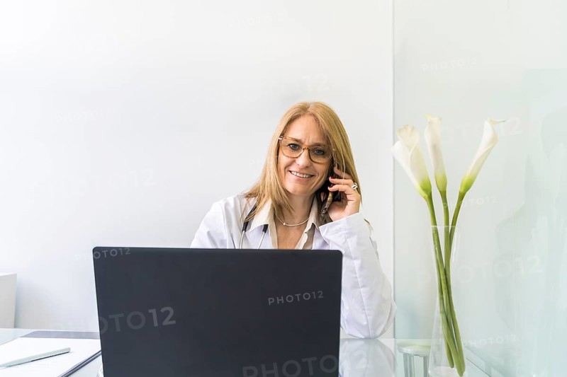 Smiling female doctor talking on the phone to a patient while looking at camera in medical office