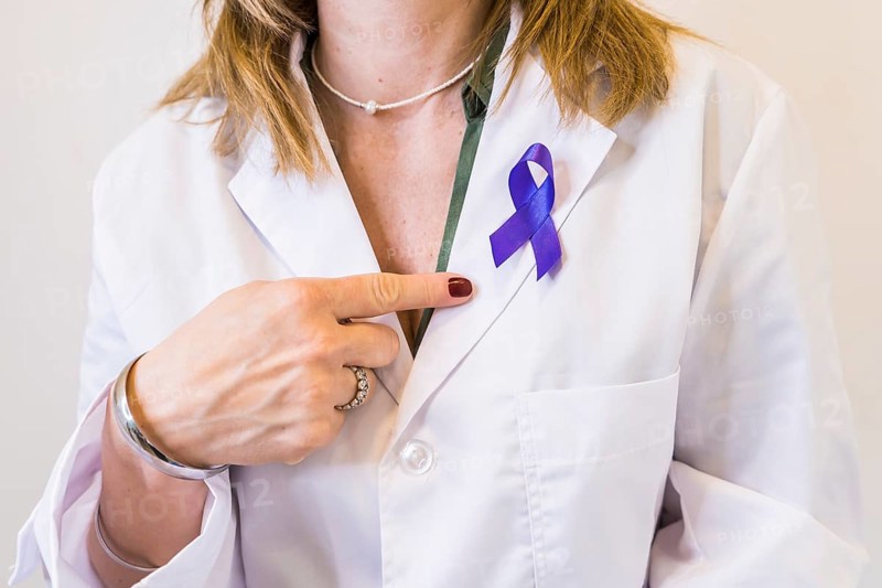 Female doctor wearing a cancer awareness ribbon while pointing at it