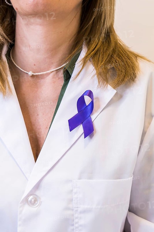Close-up of purple ribbon pinned on white lab coat of female doctor. Vertical shot