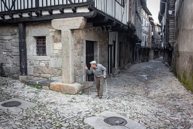 Old man with crutch and walking stick in an alley in La Alberca