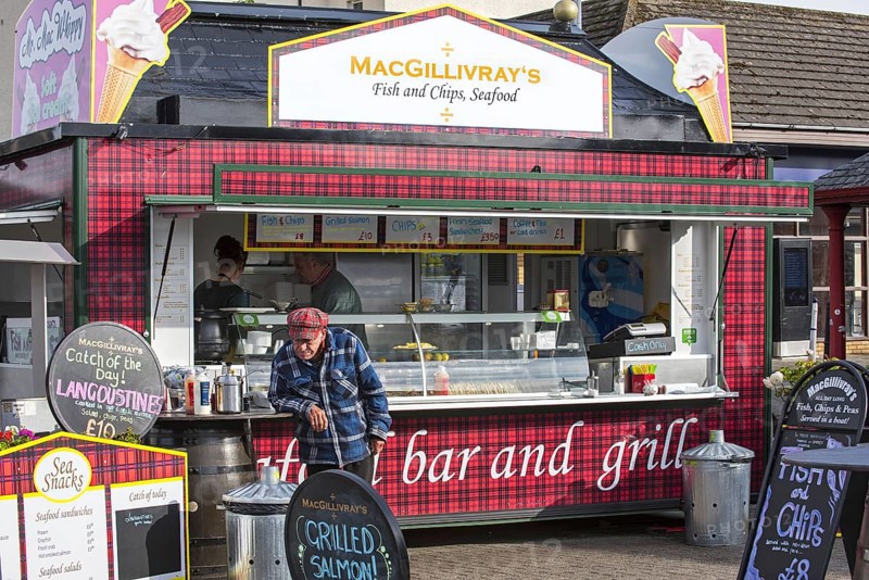 Old man in front of fish & chips and seafood stand in the city Oban