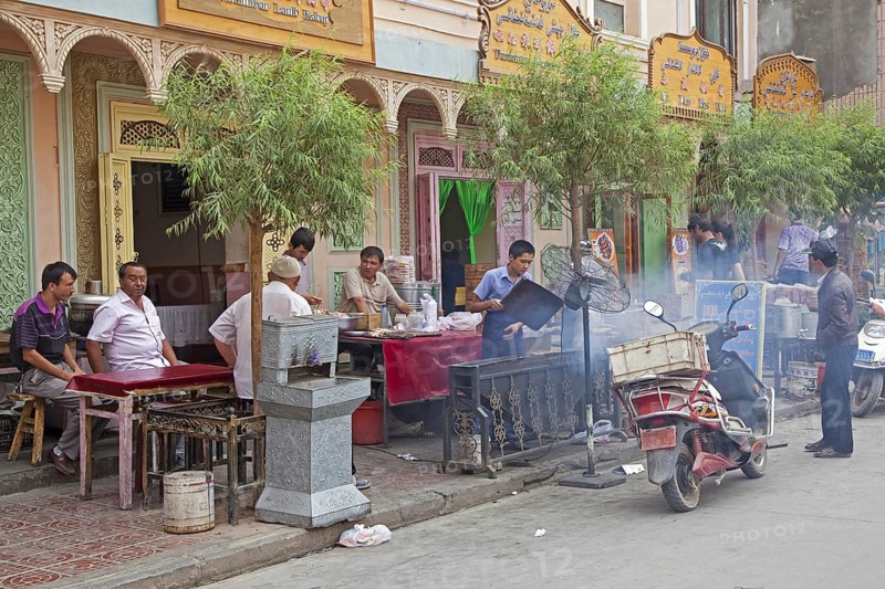 Uyghur men eating grilled meat outdoors at small traditional restaurant in the city Kashgar