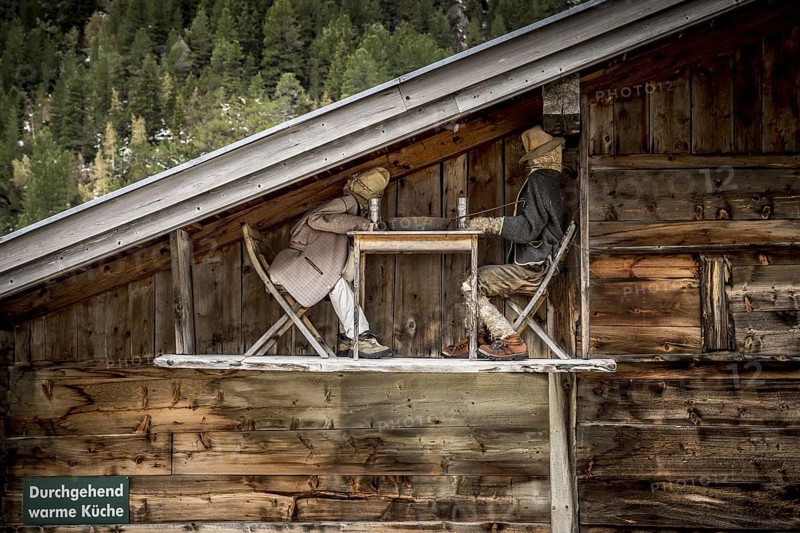 Funny scene on wooden alpine barn showing two straw figures drinking beer at a table