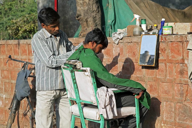 Hairdresser cutting boy's hair in the streets of Agra