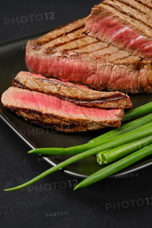 Closeup view of grilled tri-tip loin beef steaks medium rare with fresh vegetables on black background