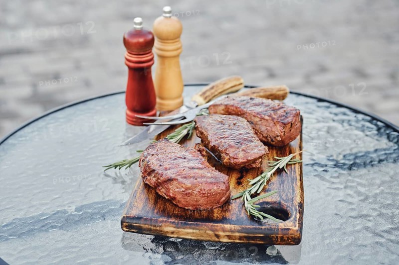 Tree juicy grilled strip steaks served on wooden cutting board