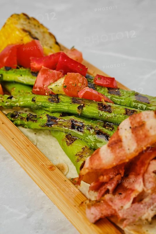 Grilled asparagus with bacon and corn on wooden serving board