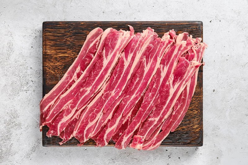 Top view of wooden cutting board with fresh raw beef bacon strips