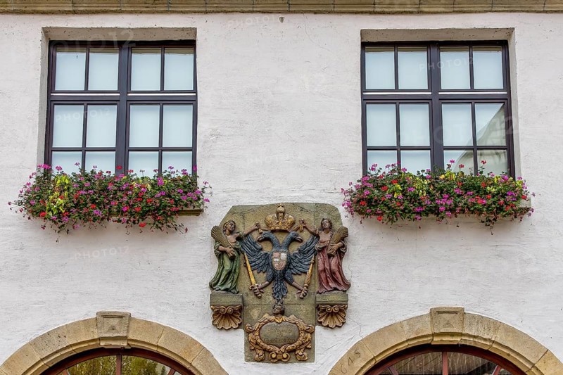 Detail of a building with two windows and coat of arms in the centre