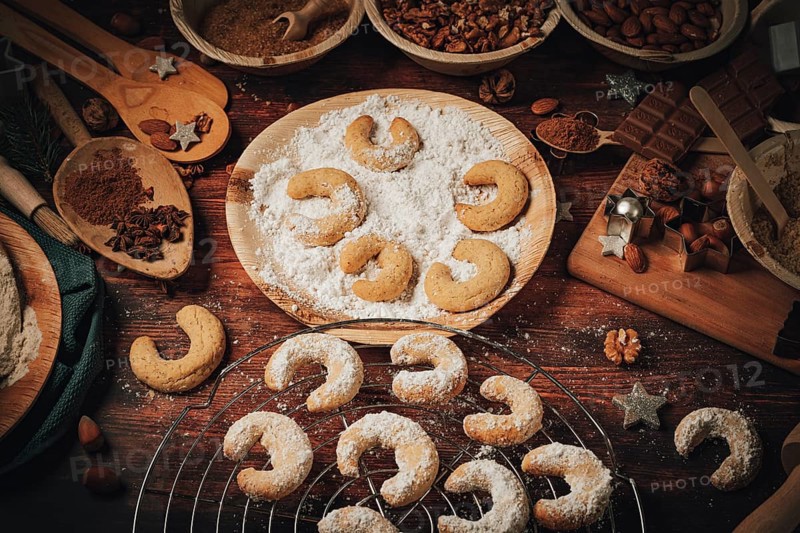 Baked vanilla crescents on a cake rack and in icing sugar