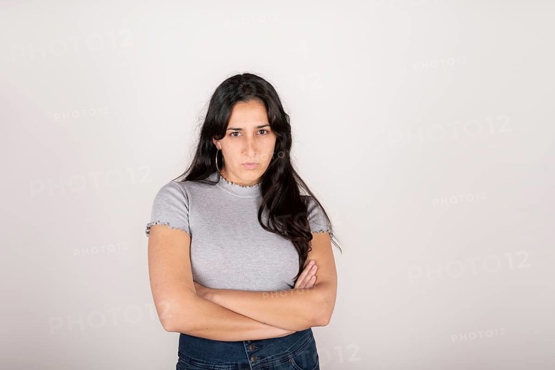Portrait of a young latin woman dressed in a grey t-shirt with her arms crossed and an angry face